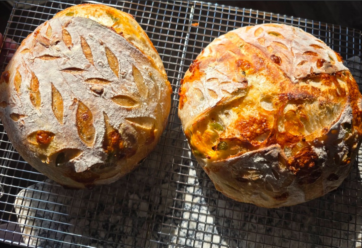 Two round sourdough loaves cooling on a rack, hand-scored with a wheat-stalk pattern